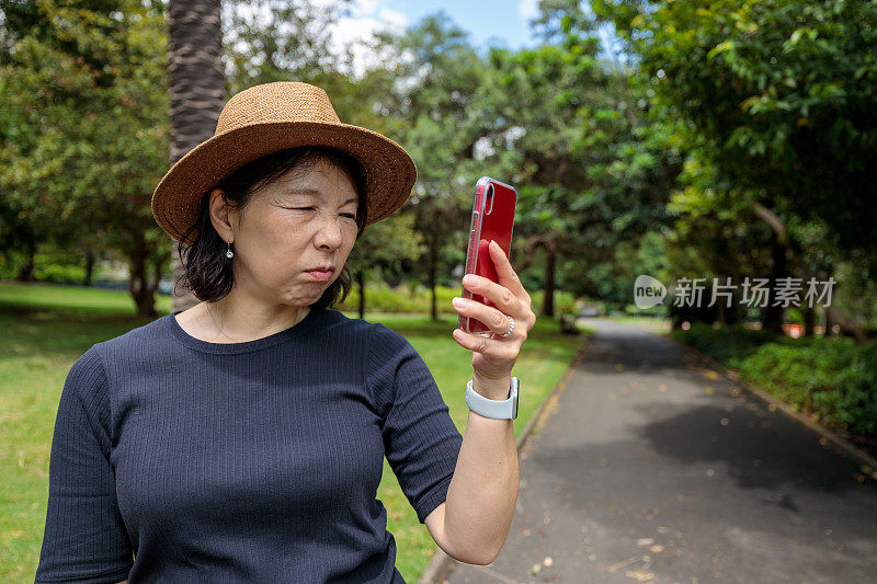 一个亚洲女人在公园里看手机，一副恼火的表情