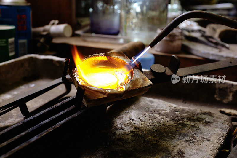 手工珠宝商在铸造一件珠宝之前，在工作台上的坩埚里加热纯银