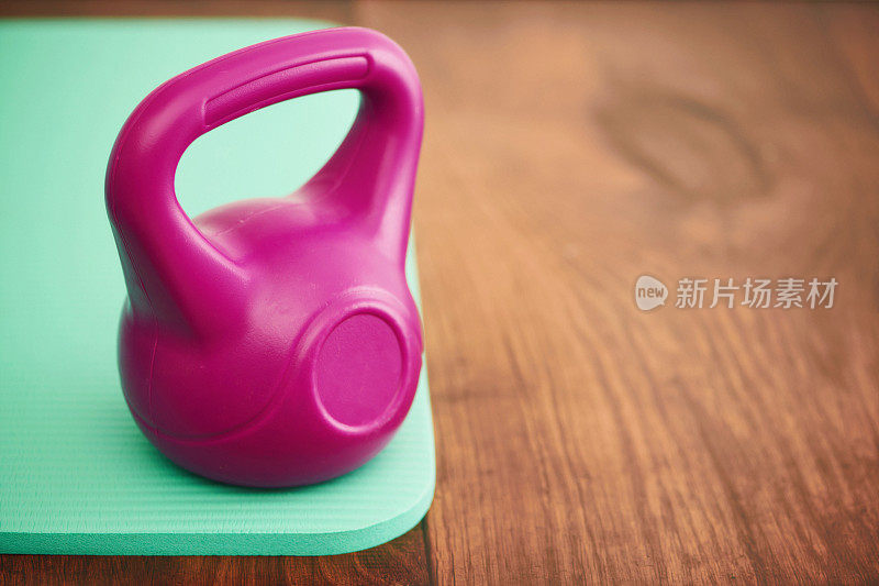 粉红色的水壶铃放在绿色瑜伽垫上的硬木地板上，还有复印空间