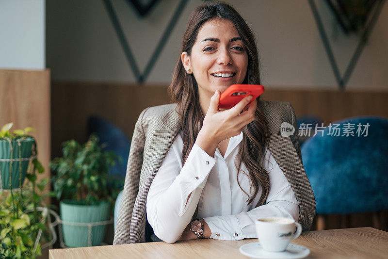 漂亮的年轻女子在咖啡馆边喝咖啡边用智能手机聊天