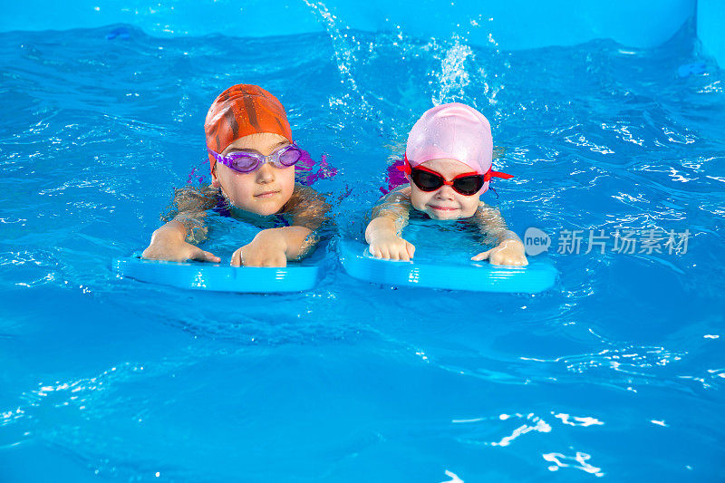 两个小女孩在游泳池里学习如何用冲浪板游泳
