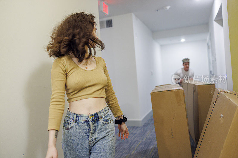 在搬迁期间，年轻女子带着纸板箱从电梯里引导她的海军士兵丈夫到他们的公寓。