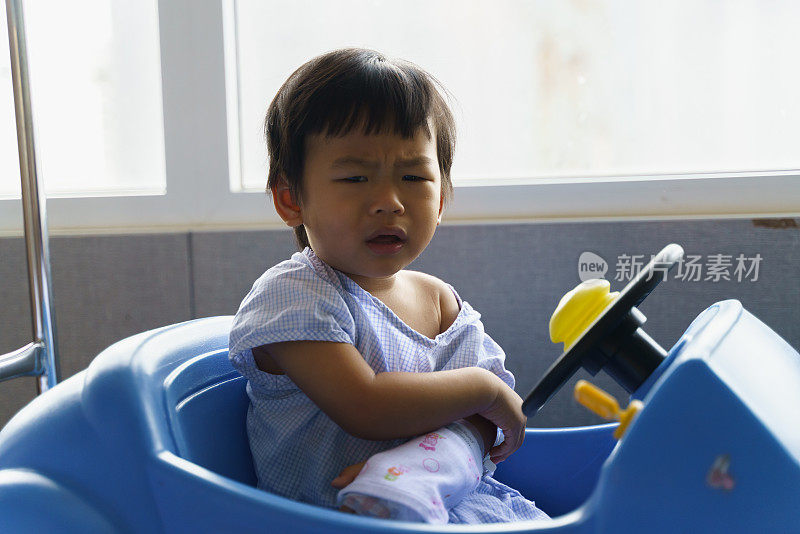 亚洲生病的小男孩在医院病房里接受生理盐水的静脉注射，在康复期间坐在医院的玩具车上。可爱的亚洲孩子感染病毒住院了。婴儿保健医疗理念。