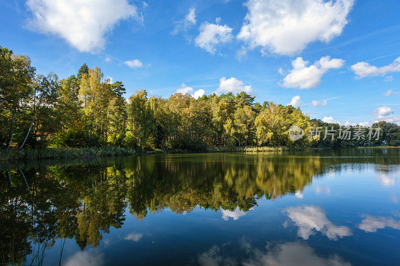 湖的自然景观，清晰度高，运动的波浪衬托着秋天的森林。云在水波上的倒影。德国。