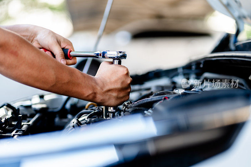 汽车修理工使用套筒扳手在车房内修理发动机，更换备件，检查汽车的里程，检查和维护服务的概念。