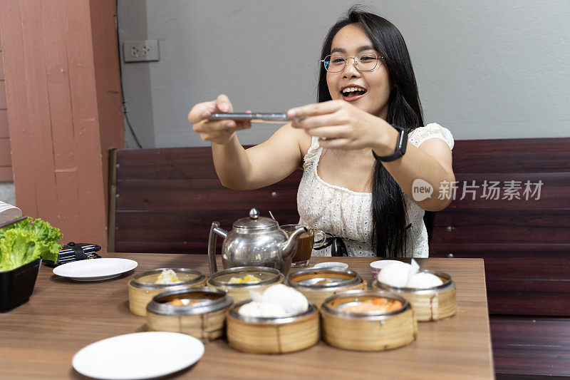 一个女人坐在桌子旁，桌上摆着各种各样的食物，包括饺子和沙拉。她正在用手机给食物拍照。