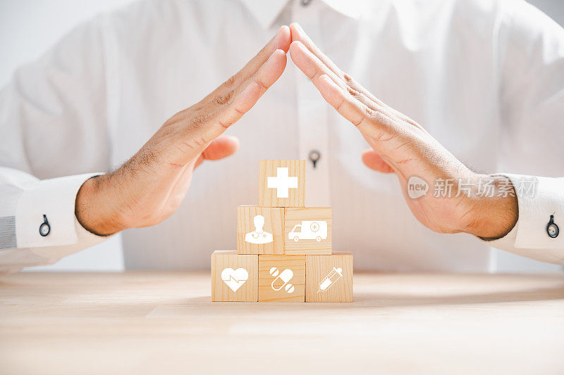 医疗保健和保险的象征性代表，通过一个医生的手在一个带有保护标志的木制立方体块。堆叠的医疗图标展示全面的医疗服务。医疗保健理念