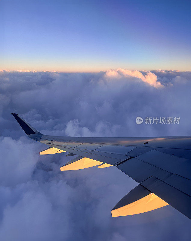 从飞机窗口看的特写图像，在云层上看到的飞机机翼，蓬松的白云，小翼和板条，橙色的日落，重点在前景