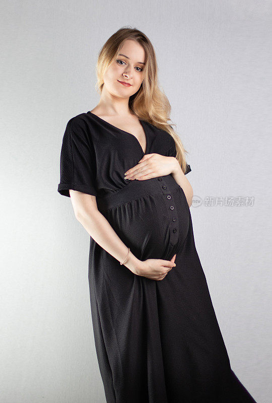 这是一幅漂亮的年轻孕妇肖像，她有着金色的长发，背景是普通的中灰色。