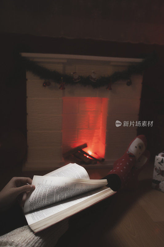 年轻女子在圣诞树下看书，在壁炉旁暖腿