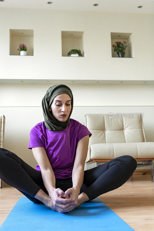 年轻的穆斯林妇女戴着头巾在家笔记本电脑前做伸展运动，在客厅里训练，观看在线教程，宗教非洲妇女享受健康的生活方式