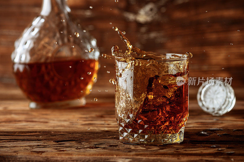 白兰地一杯白兰地、威士忌或白兰地，洒下一块冰块，放在棕色的木桌上，以一瓶含酒精饮料为背景