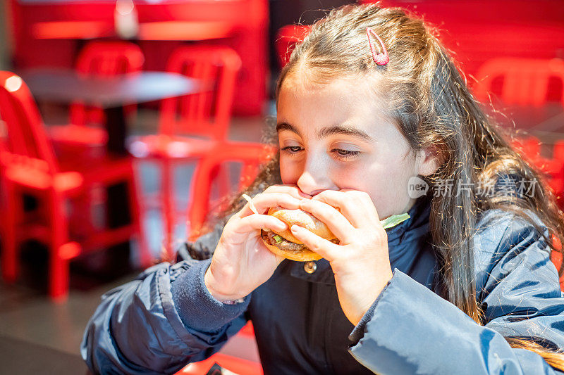 对待自己(购物)。一个快乐的小女孩在快餐店里吃起司汉堡