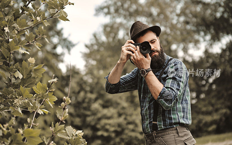 一个留着胡子的英俊的年轻人正在一个绿色的公园里拍照。