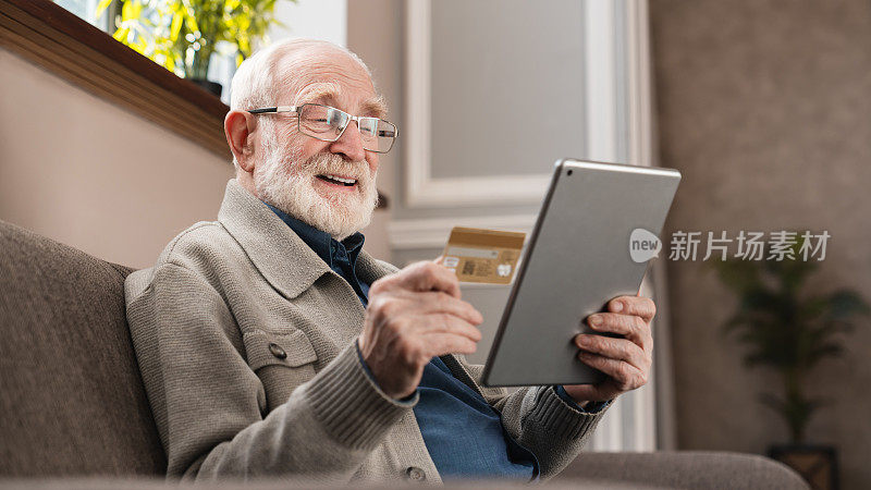 现代老爷爷在家里用平板电脑和信用卡在线购物。老爷爷用数码平板电脑网购。老人在网上支付账单。