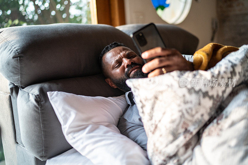 一个成熟的男人躺在床上玩智能手机