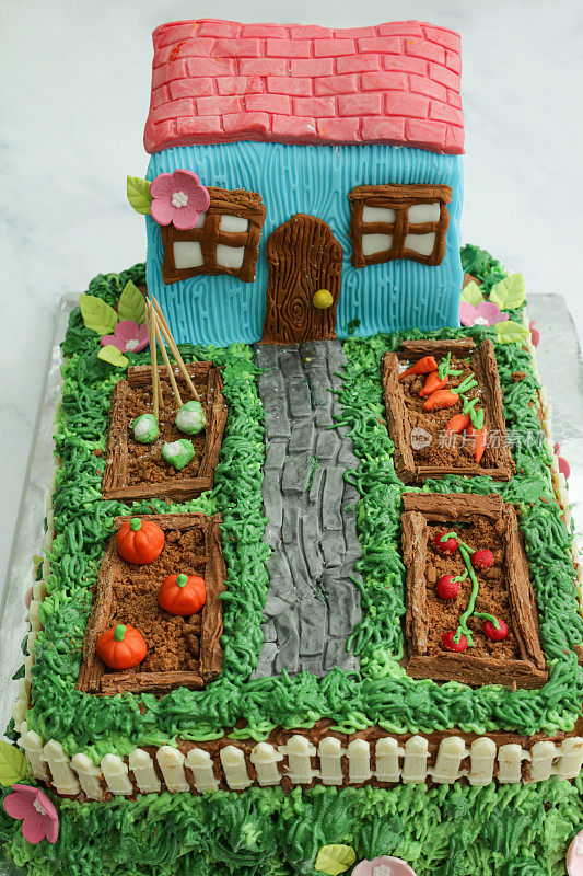 分层的，自制的，装饰的蛋糕设计成小屋和花园，有凸起的蔬菜床，黄油糖霜草，巧克力片和饼干屑土壤菜地，方糖糖霜南瓜，西红柿，花椰菜和胡萝卜，高架视野