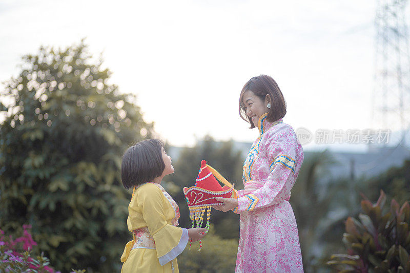 亚洲华人母亲和女儿在后院穿着传统服装庆祝中秋节。