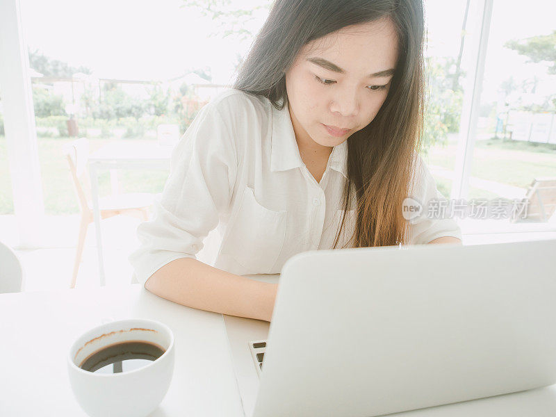年轻的亚洲女性工作认真使用笔记本电脑和咖啡饮料在咖啡馆。