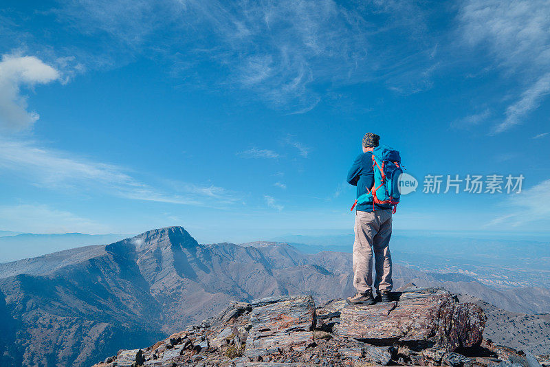 成功的年长的登山者是双手交叉站在山顶上欣赏风景