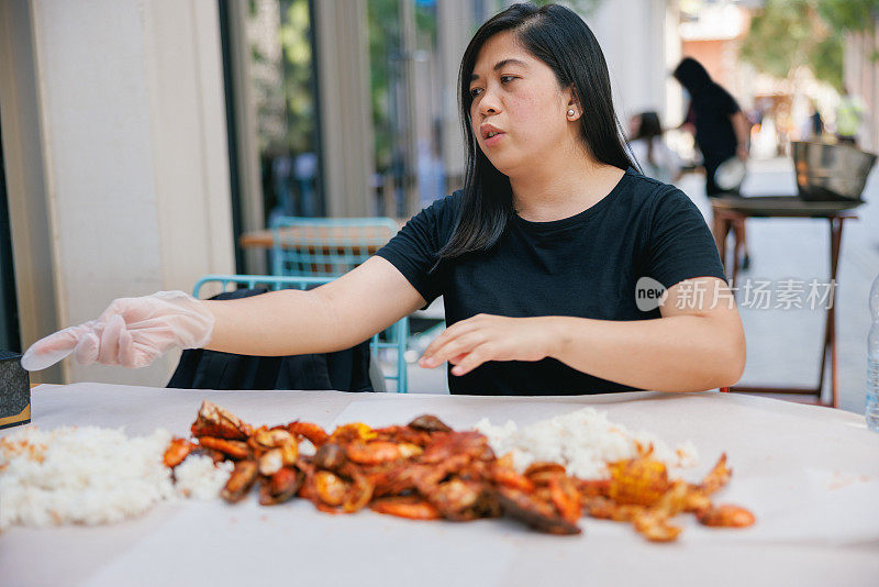 妇女坐在餐桌上戴着手套吃海鲜和米饭堆