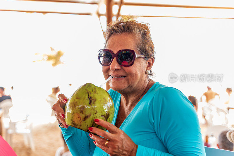 迷人的西班牙裔老年妇女喝椰子水