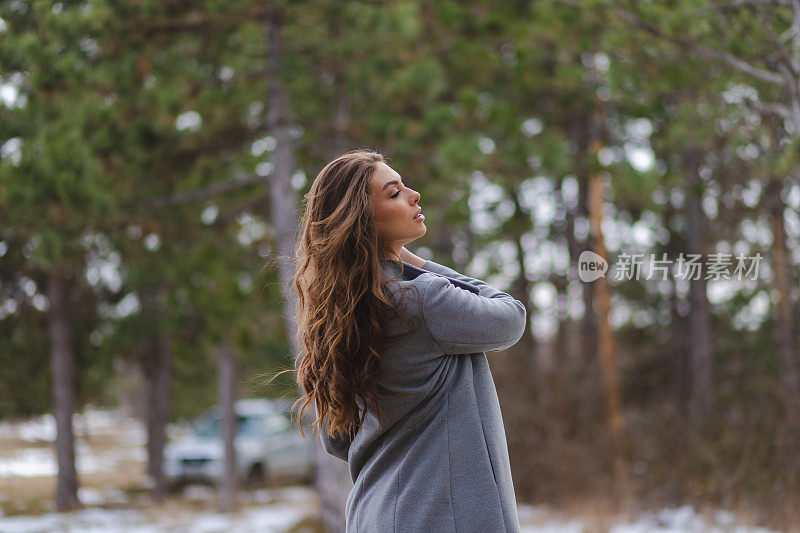 一幅年轻女士的肖像，穿着灰色外套和黄色毛衣在森林里