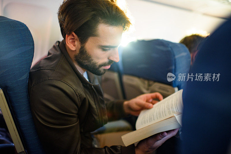 一个年轻人在飞机上看书。