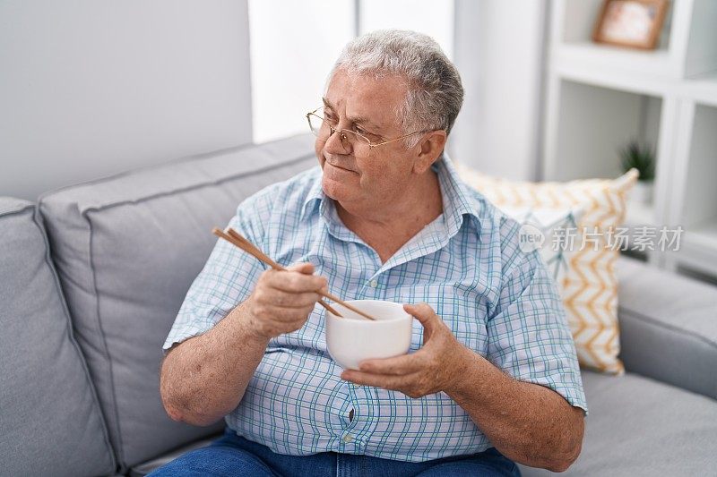 中年白发男人坐在家里的沙发上吃中餐
