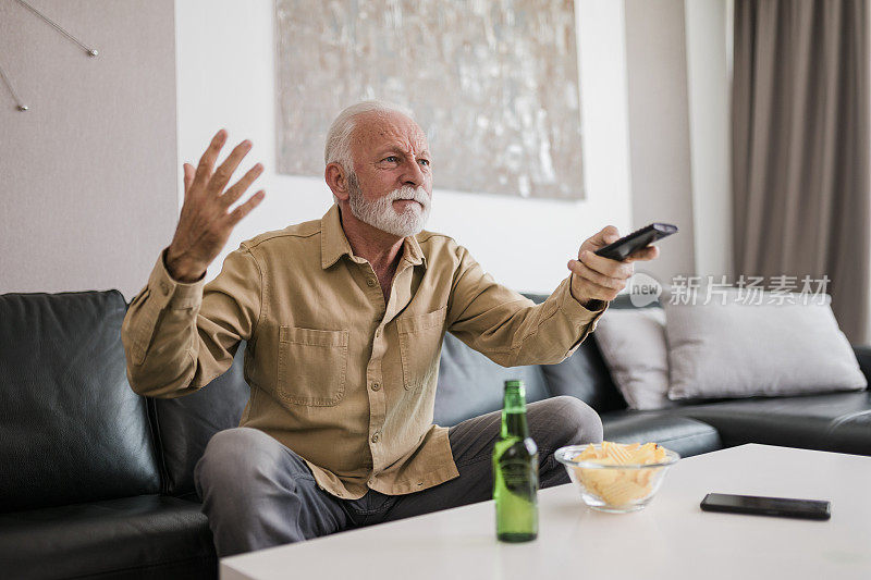 压力和兴奋的足球迷老男人看电视上的足球比赛在家里的沙发