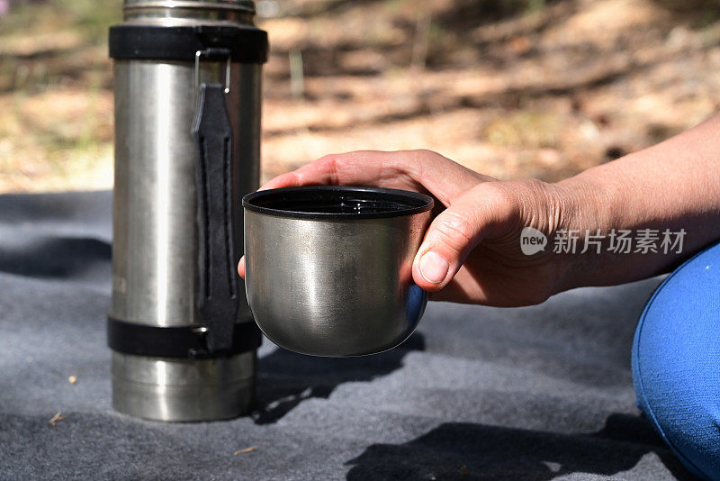 野餐时，森林里妇女的手从保温瓶里倒茶