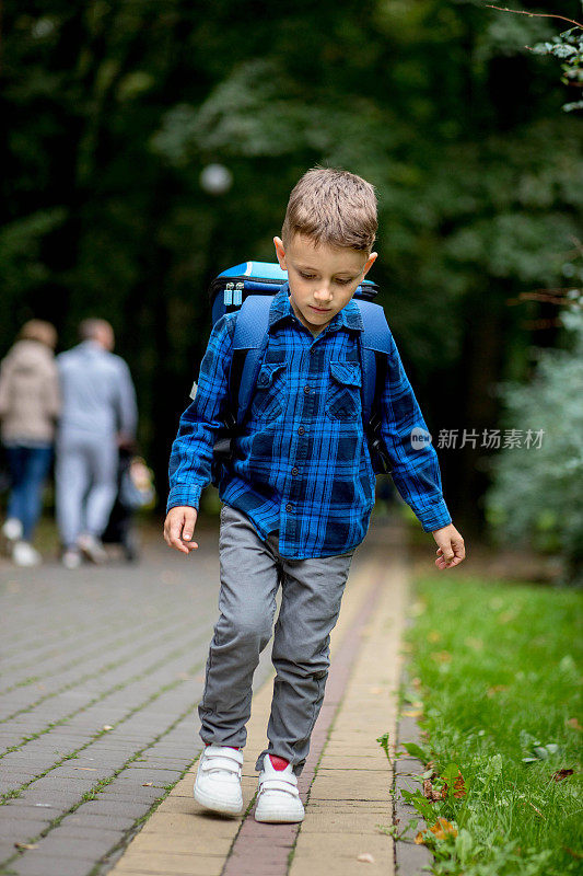 一个带着蓝色背包的学龄男孩去公园上学