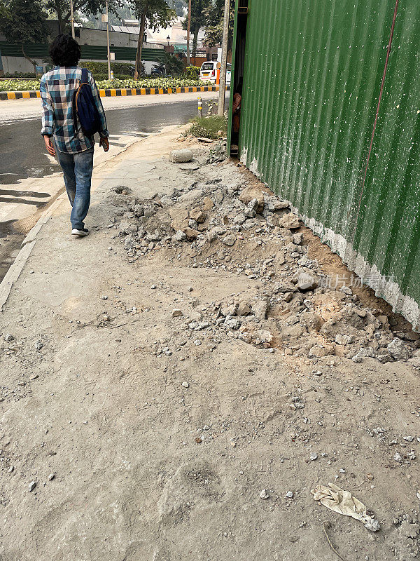 图像无法识别的印度人走在危险的人行道上，建筑工地的障碍，废墟绊倒危险，后视图