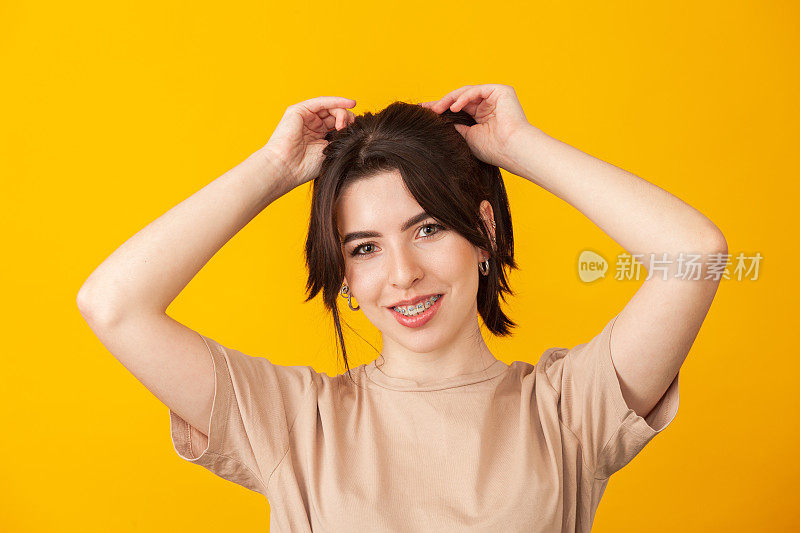 一个快乐的20岁白人女性，黑色头发在黄色背景下米色t恤的工作室肖像