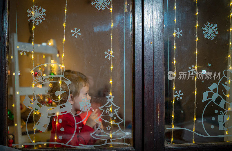 小兴奋的孩子在圣诞夜等待着圣诞老人。一个学龄前的男孩望着窗户，希望在新年的夜晚魔法和礼物