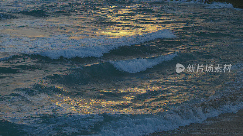 黑色海面上的波浪，金色的夕阳映在水面上
