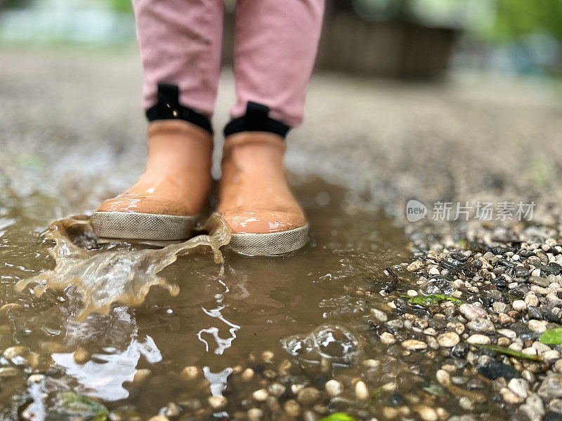 穿着胶靴的孩子的脚，一个孩子站在水坑里，用脚泼水，背景