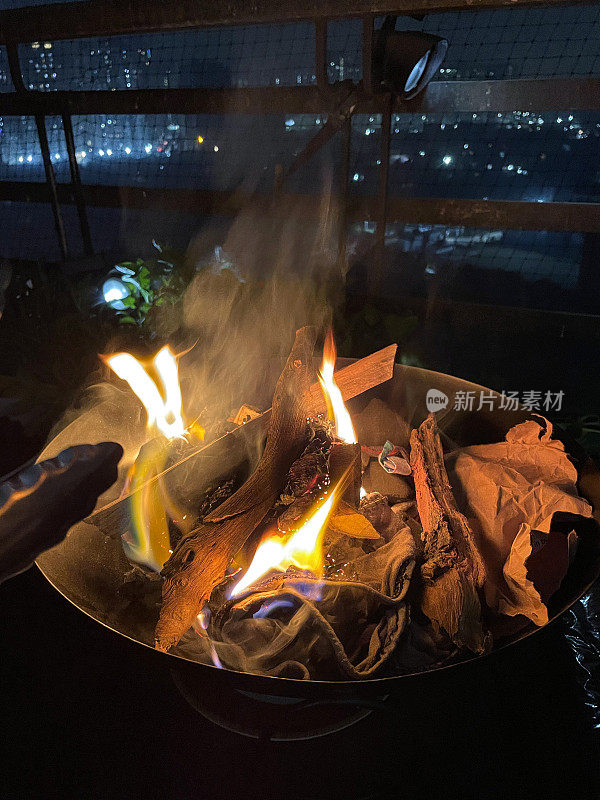 在晚上，一个充满了燃烧的煤炭和木材的火坑的图像。圆形烧烤架里的木炭在黑暗中发出红光