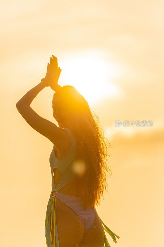日落时分，沙滩上阳光灿烂。美丽的白人女子在海滩上的比基尼与精湛的日落和阳光在后面