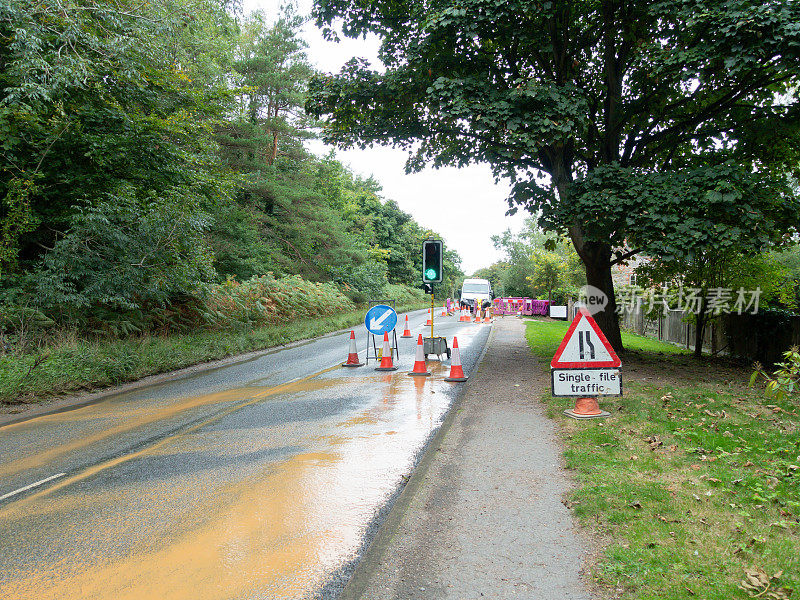 道路工程交通信号灯锥形锥和漏水，英国农村的一条乡村道路上，工人们正试图修复众多漏水中的一个，这些漏水浪费了大量的水。