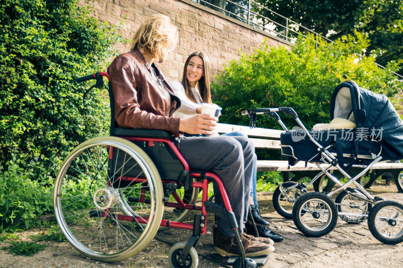 年轻的父母坐着轮椅推着婴儿车在公园里