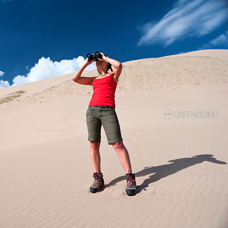 一个年轻女子正在沙漠中用双筒望远镜看东西