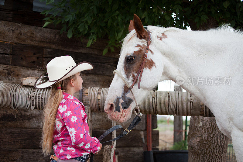 戴着牛仔帽的小女牛仔和她的马说话