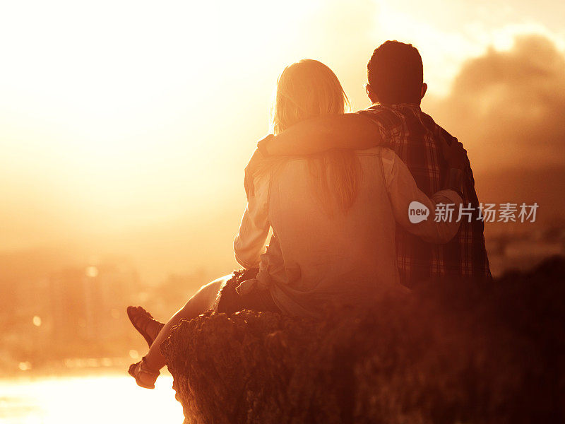 一对相爱的夫妇欣赏日落的后视图。