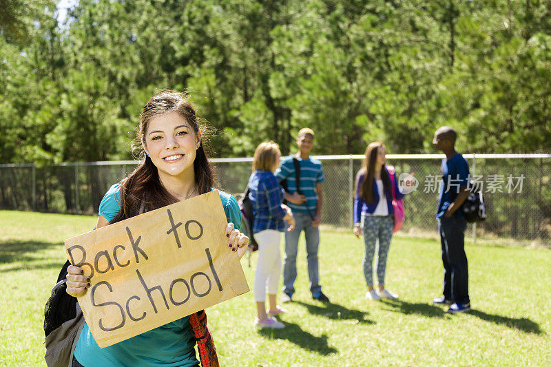 拉丁少女举着“回到学校”的牌子。朋友的背景。