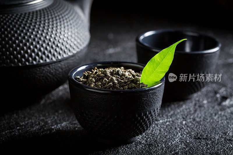 新鲜绿茶，茶壶和杯子放在黑岩上