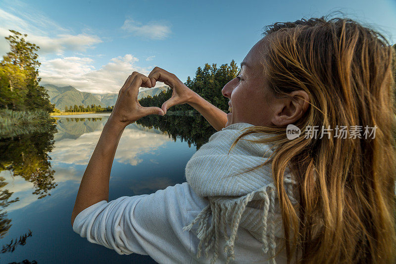 女人在山湖景观上做心形指架