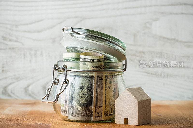 玻璃罐中的美元孤立在木制背景和小木屋。存钱买新房子。