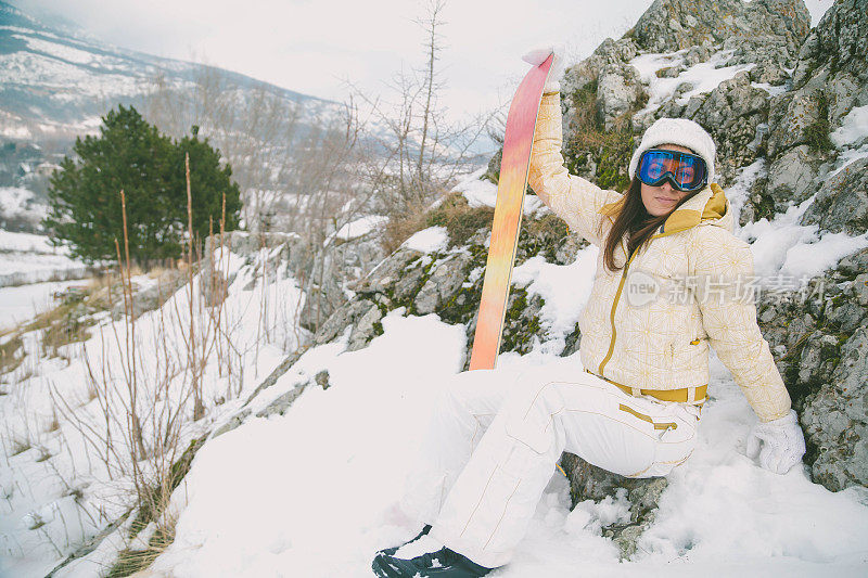 近景美丽的年轻女子在冬天的衣服站在一边，手拿木棍的背景雪山