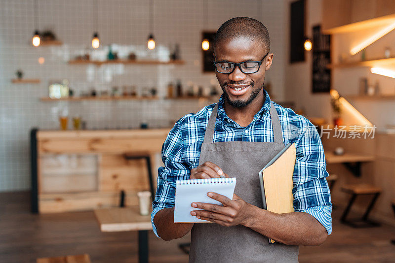 英俊微笑的非裔美国侍者在咖啡店用记事本和平板电脑点菜